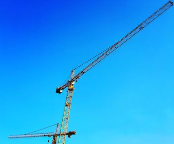 Low angle view of crane against clear blue sky