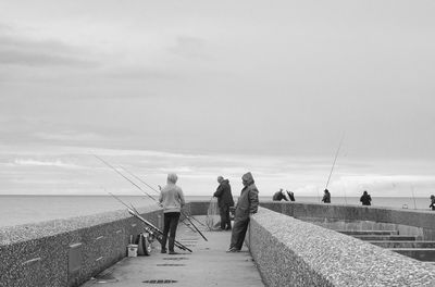 Rear view of people fishing on sea against sky