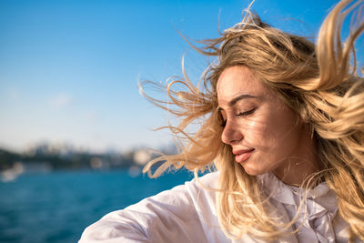 Close-up of beautiful woman with tousled hair against clear blue sky