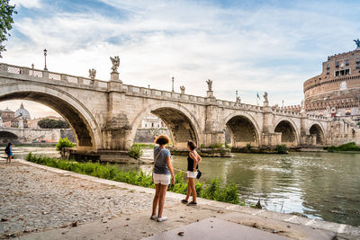 People standing at bridge in city against sky