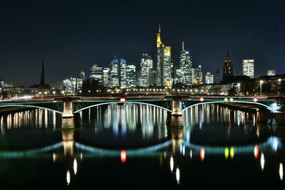 Illuminated bridge over river by buildings against sky at night