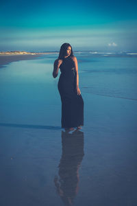 Young woman standing at beach against sky