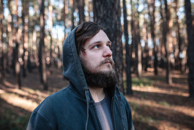 Thoughtful man wearing hooded jacket in forest