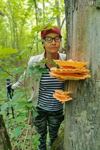 Portrait of young woman standing by tree trunk