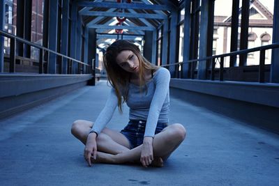 Thoughtful young woman looking away while sitting on bridge