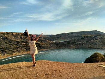 Full length of woman with arms raised standing at gnejna bay