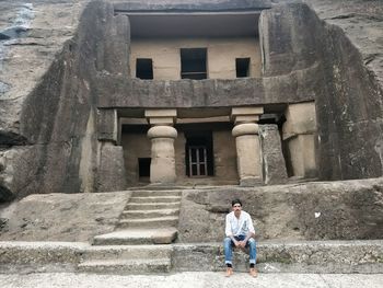 Full length portrait of man sitting against old ruins