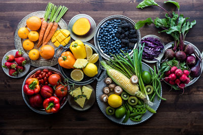 Various fresh organic fruits and vegetables in rainbow colours against a dark wooden background.