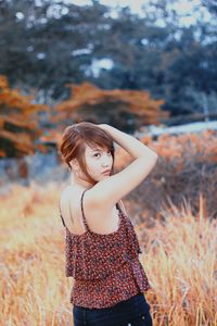 Side view of young woman looking away while standing on grassy field