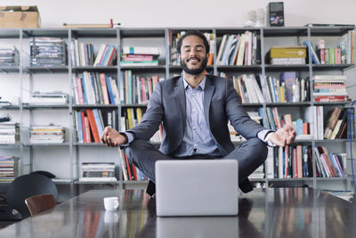 Young businessman sitting in office meditating in front of laptop