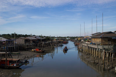 Sailboats moored on river by houses against sky
