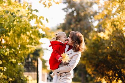 Happy mom and child are walking and having fun playing with autumn leaves in the fall park outdoors