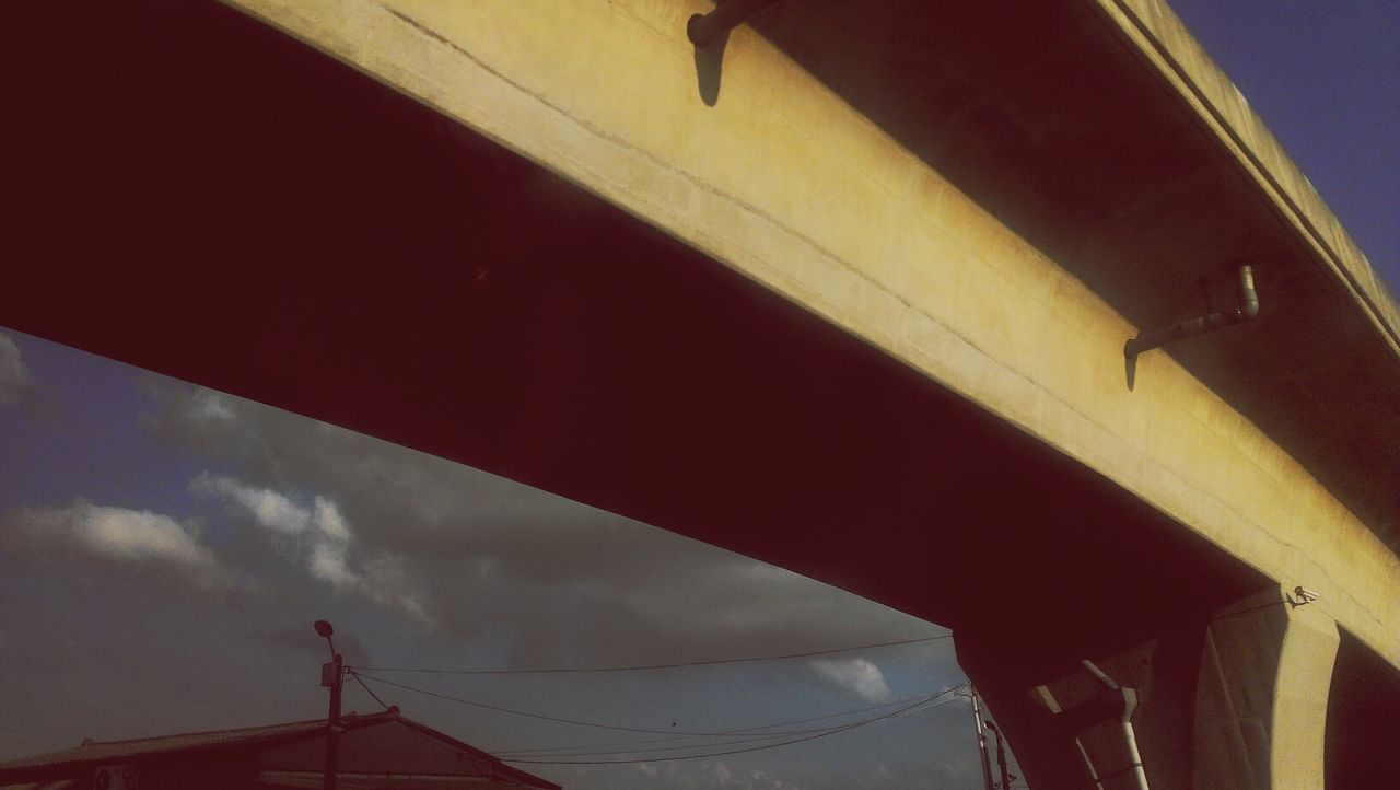 low angle view, built structure, architecture, sky, cloud - sky, building exterior, connection, outdoors, part of, no people, day, sunlight, street light, transportation, lighting equipment, cloud, bridge - man made structure, railing, silhouette, cloudy