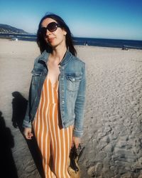 Young woman wearing sunglasses standing on beach against sky