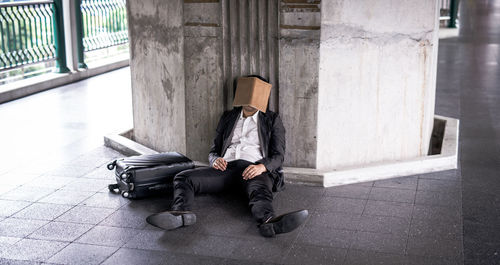 Tired businessman with book on face leaning against wall in corridor