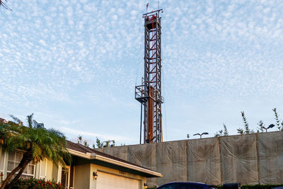 Low angle view of crane by building against sky