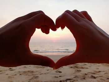 Close-up of couple making heart shape against sky during sunset