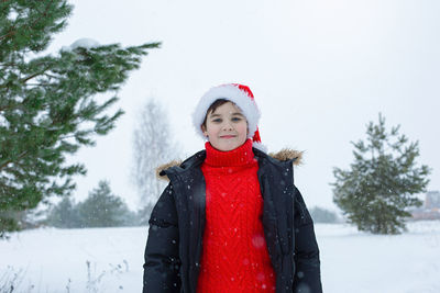 Portrait of cute teenager in a dark jacket and a red sweater, a red hat stands in the winter 