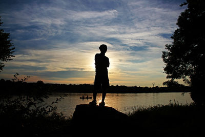 Silhouette man standing by lake against sky during sunset