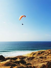 Low angle view of woman paragliding above sea against clear sky