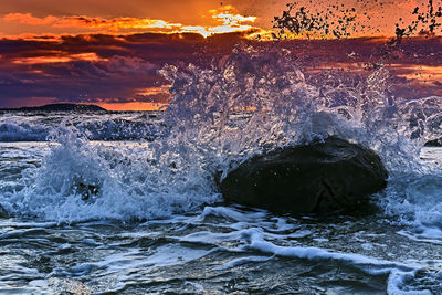 Water splashing on rocks at sea shore against sky