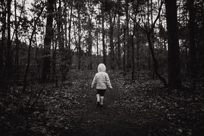 Rear view of girl wearing hooded shirt while walking in forest