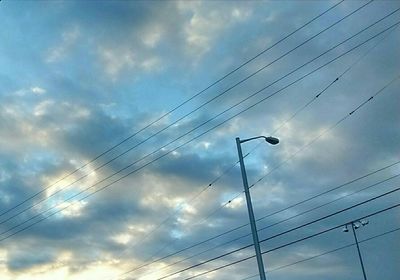 Low angle view of electricity pylon against cloudy sky