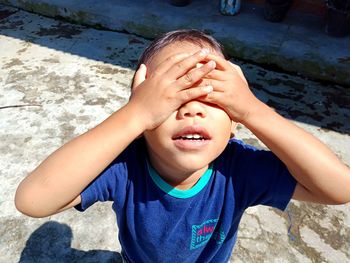 High angle view of boy covering eyes while standing on footpath