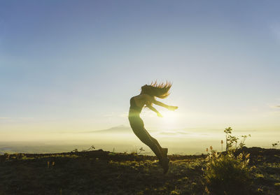 Rear view of woman with arms raised standing against sky during sunset