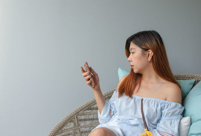 Woman using smart phone while sitting against wall