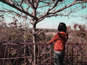 Rear view of woman standing by railing against bare trees