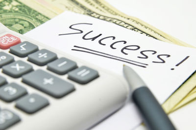 Close-up of success text on paper with calculator and paper currencies