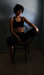 Full length of woman sitting on chair against wall