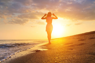 Female silhouette, rear view, with hands raised to the hat and hair flowing. seascape during golden