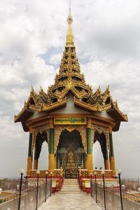 Golden gate of temple building against cloudy sky