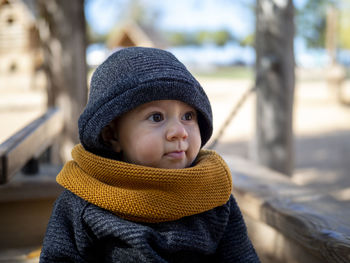 Close-up of cute girl wearing sweater and knit hat sitting at park