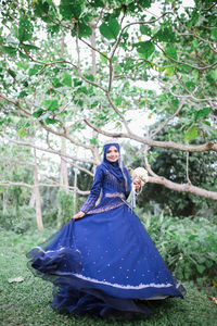 Portrait of smiling bride in traditional clothing dancing against plants at park