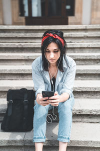 Young woman using phone while sitting on staircase