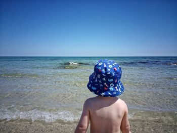 Rear view of shirtless man on beach against clear sky