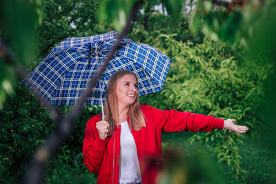 Smiling young woman under umbrella standing in forest during rainy season