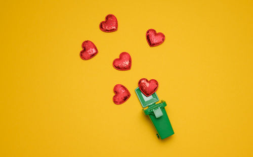 Red hearts and a miniature plastic box for collecting garbage on a yellow background