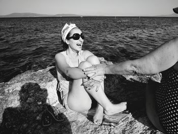 Young woman wearing sunglasses sitting on sea against sky