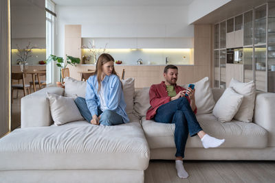 Cheating husband. arrogant man texts mistress on messenger, ignores angry and mad wife on sofa