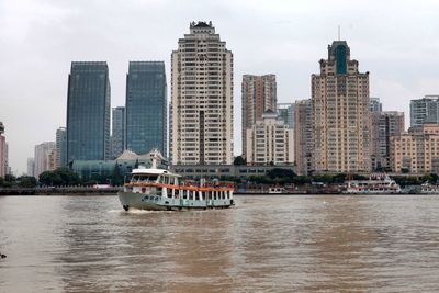 Boats in river by buildings against sky in city