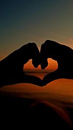 Close-up of silhouette hand holding heart shape against sky during sunset