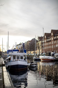 Boats moored in canal by buildings against sky