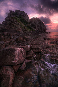 Rock formation in sea against sky during sunset