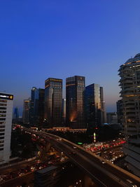 Traffic on road by illuminated buildings against clear blue sky