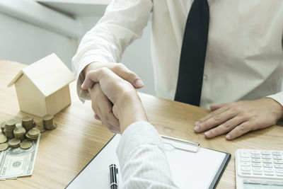Midsection of businessmen shaking hands over desk