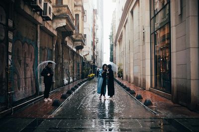 People walking on wet street amidst buildings during rainy season